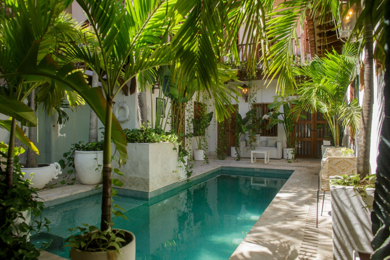 Casa Palmas courtyard pool viewed through lush banana palms with seating lounge and upper colonial balcony