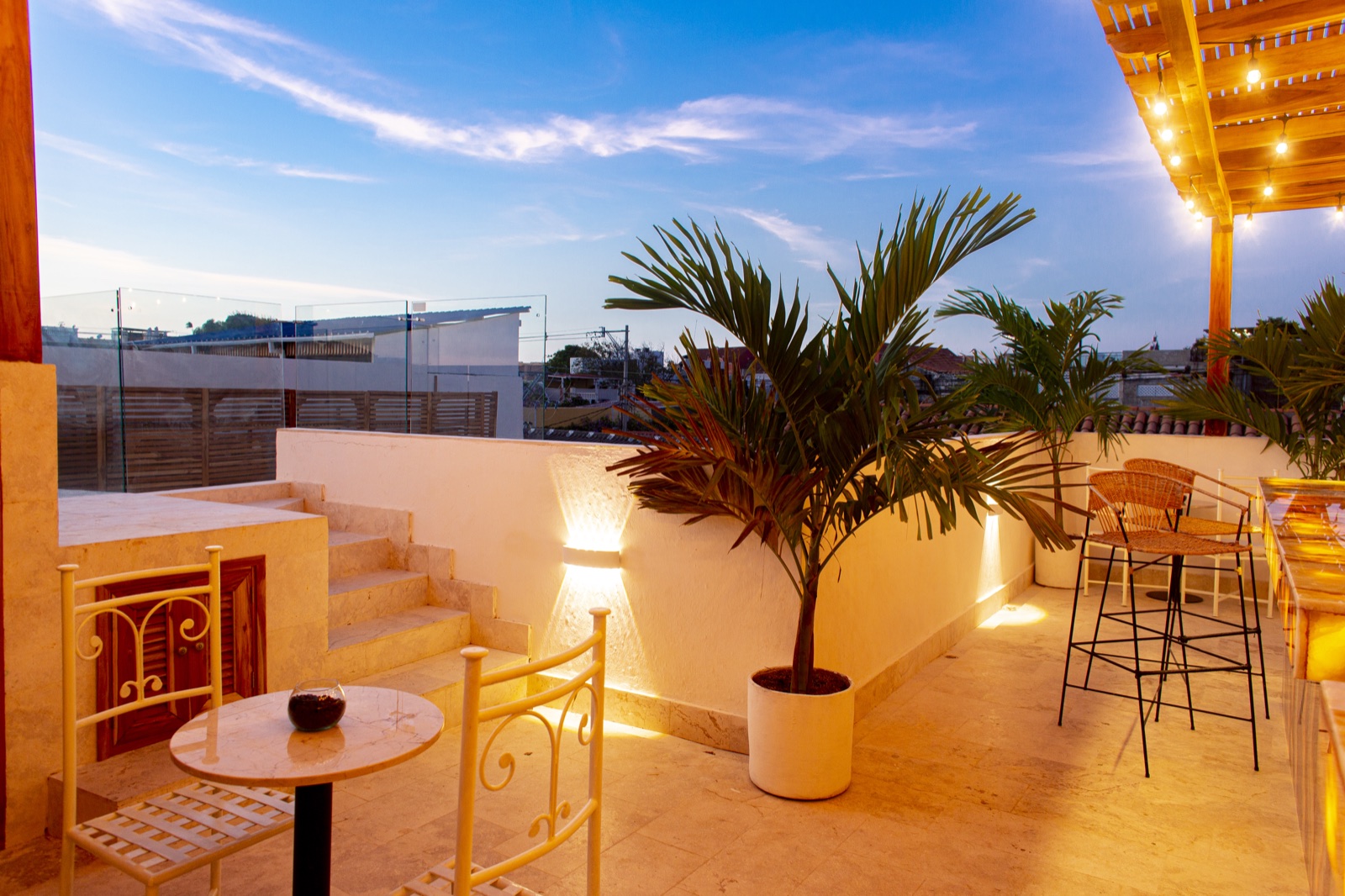 Casa Palmas rooftop lounge terrace at dusk with travertine flooring, tropical palms, and panoramic city views
