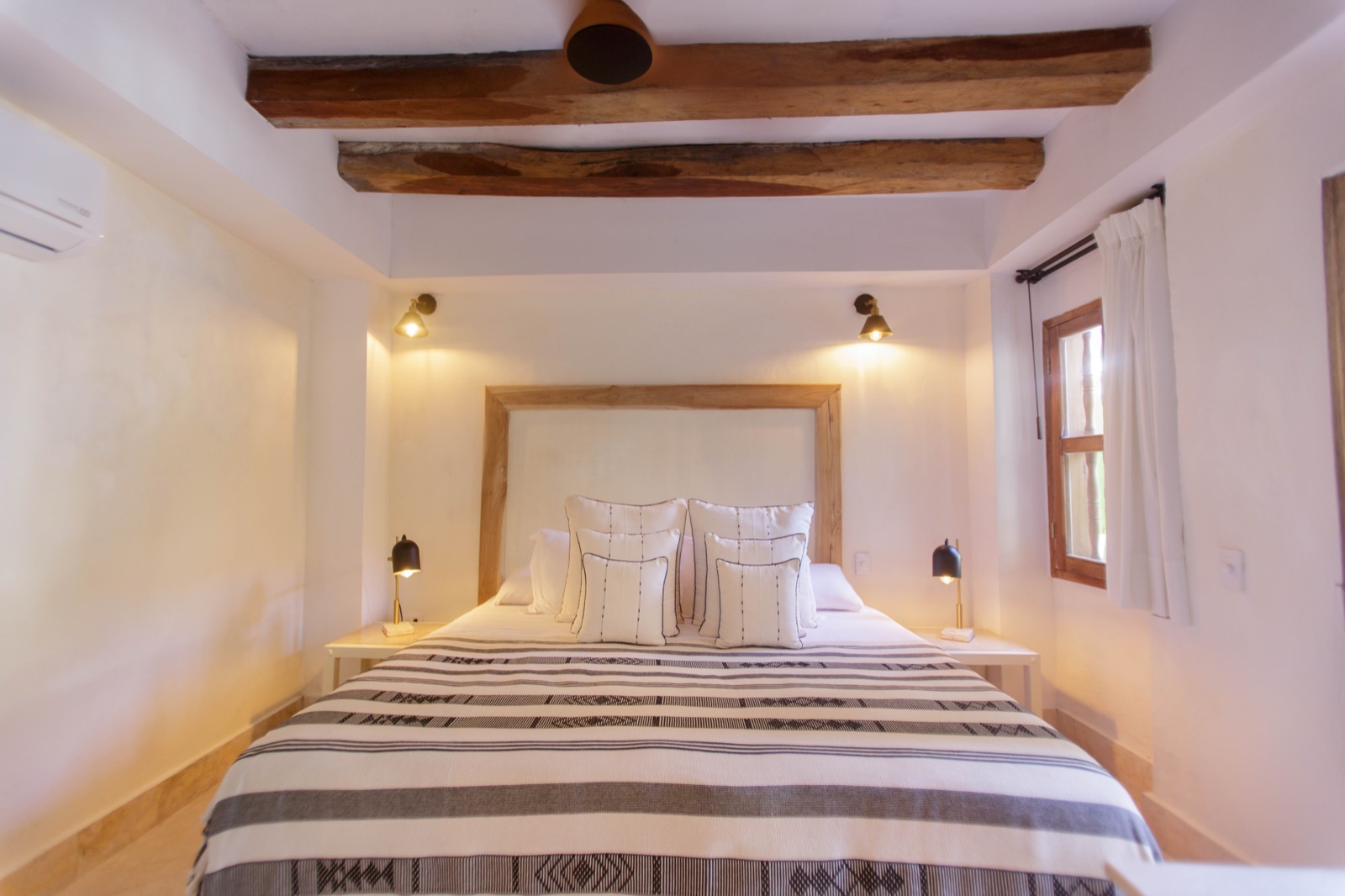 Casa Palmas Superior Room with king bed, artisan striped linens, paired brass sconces, and original colonial wood ceiling beams