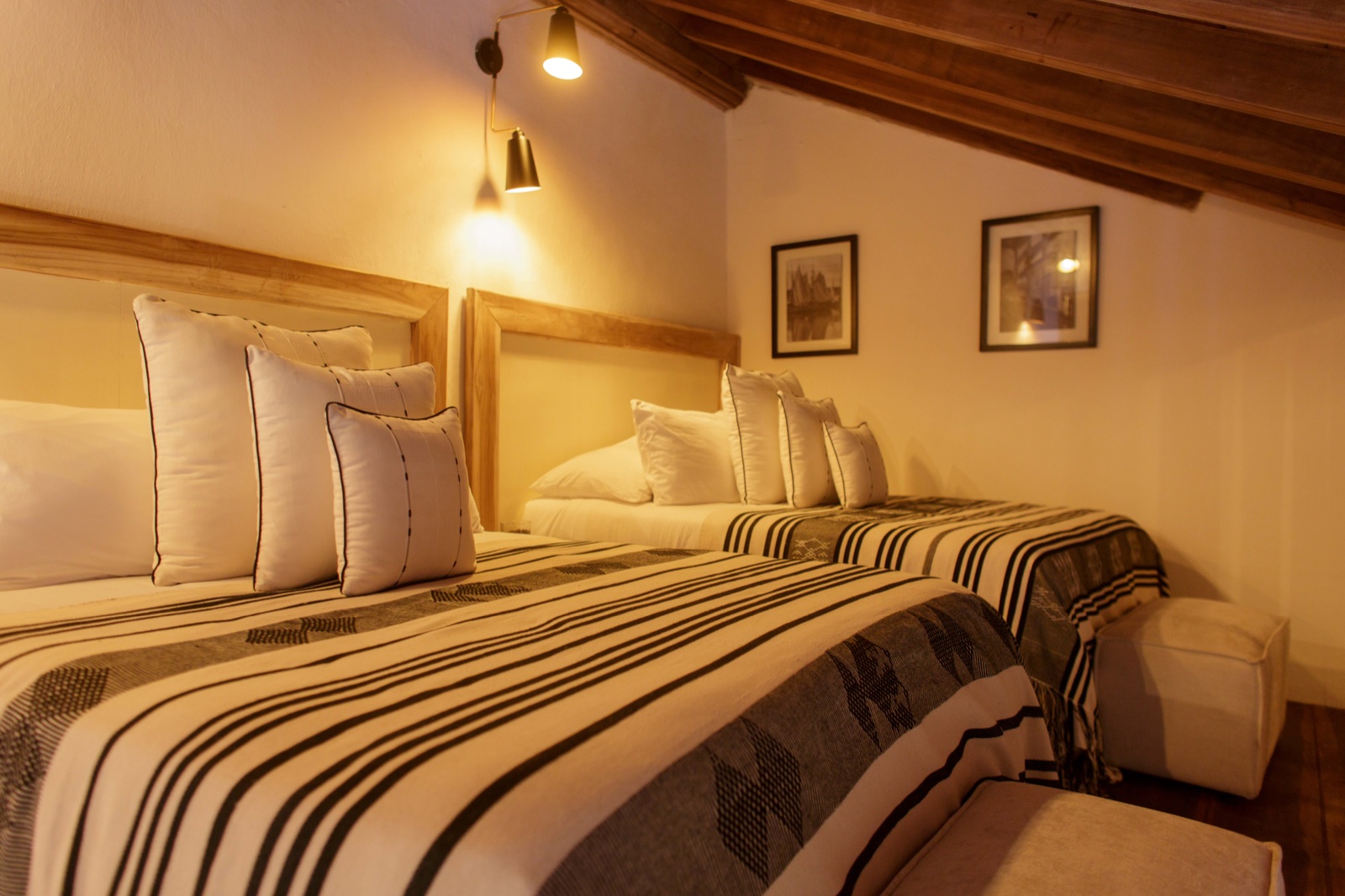 Casa Palmas twin bedroom under a sloped colonial wood-beam ceiling with dual queen beds and warm amber lighting